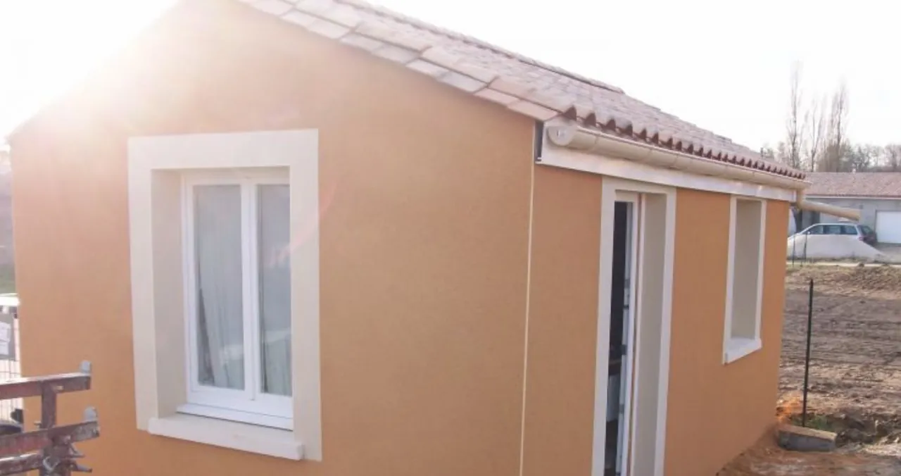 Petit bâtiment aux murs enduits orangé, fenêtres soulignées d’encadrements clairs, toit en tuiles