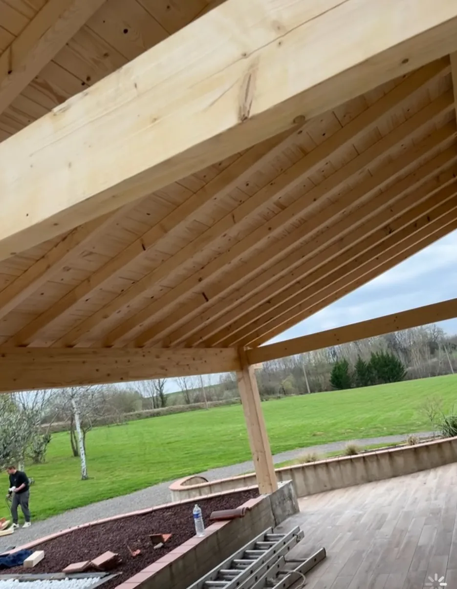 Dessous d’un auvent en bois neuf : chevrons et voliges, poteau et poutre, jardin et terrasse autour