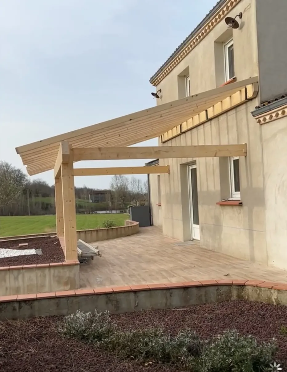 Ossature en bois d’un auvent contre la façade d’une maison : poteaux, poutres et chevrons posés, avant la couverture