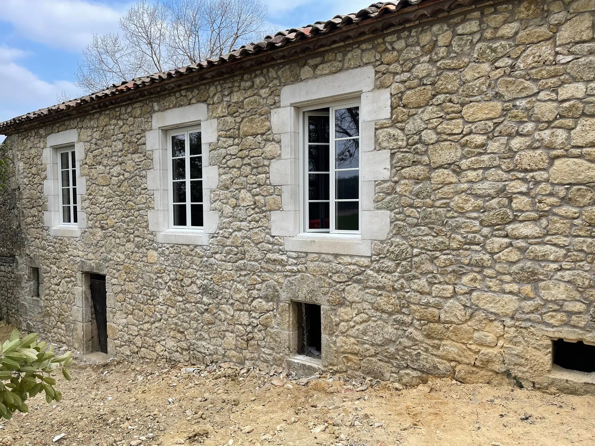 Façade en pierre rénovée : moellons rejointoyés, encadrements de fenêtres en pierre de taille, fenêtres neuves