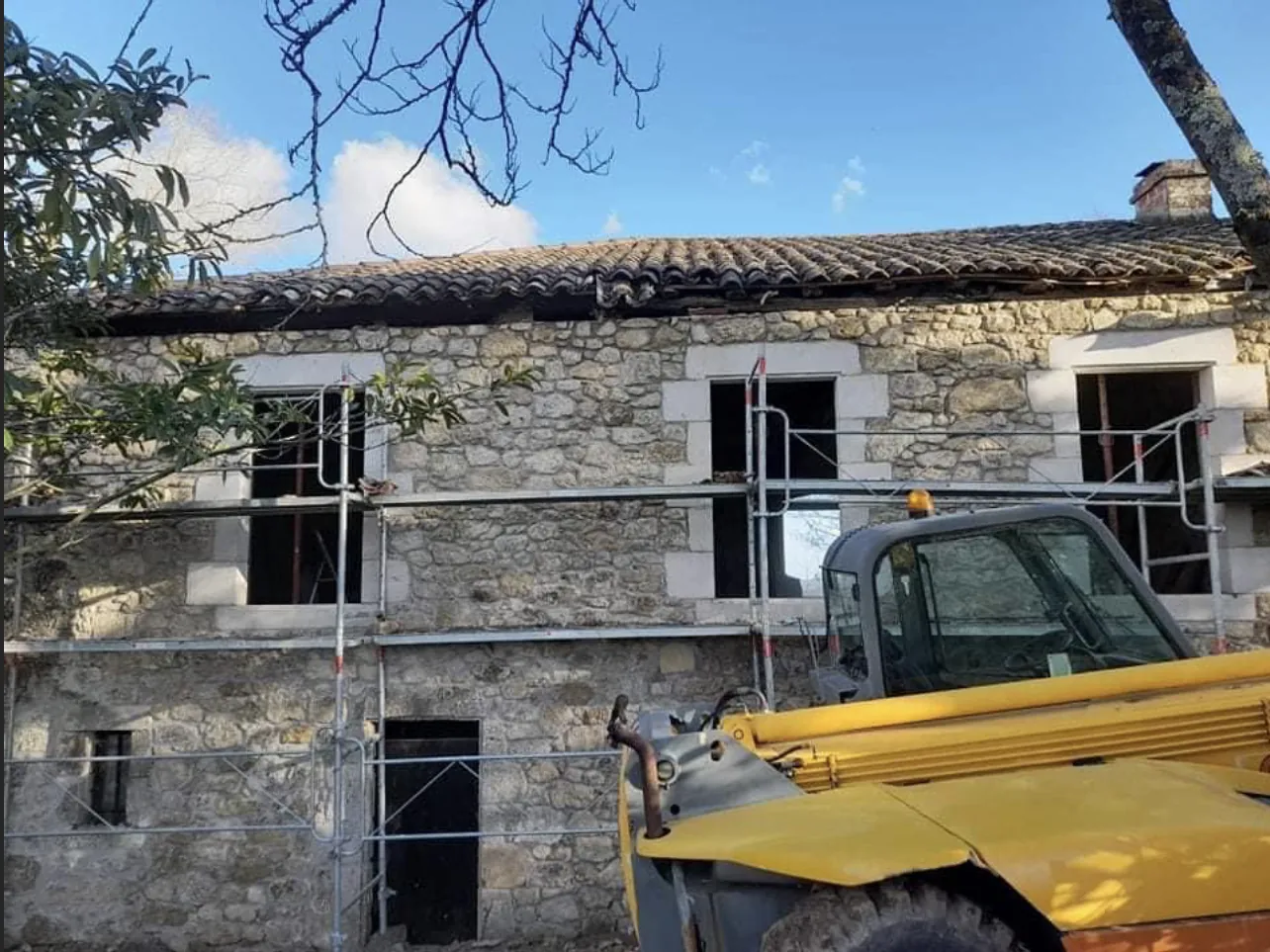 Façade en pierre pendant les travaux : échafaudage devant les ouvertures aux encadrements de pierre, chariot élévateur au premier plan