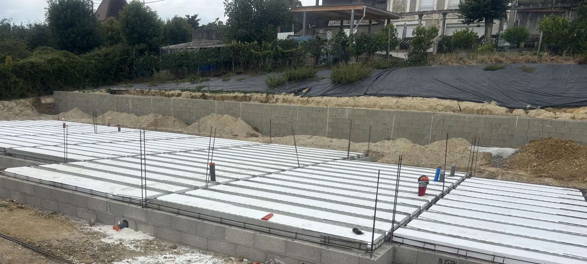 Plancher sur vide sanitaire d’une grande maison neuve : poutrelles et entrevous blancs posés sur le soubassement en blocs béton, gaines rouges en attente au premier plan
