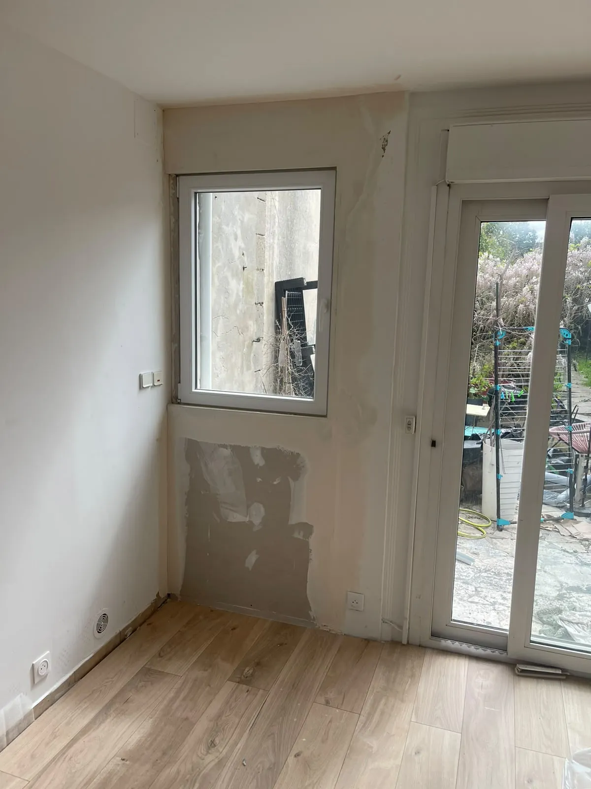 Pièce en finition : sol façon parquet posé, mur sous la fenêtre repris à l’enduit, porte-fenêtre sur la cour