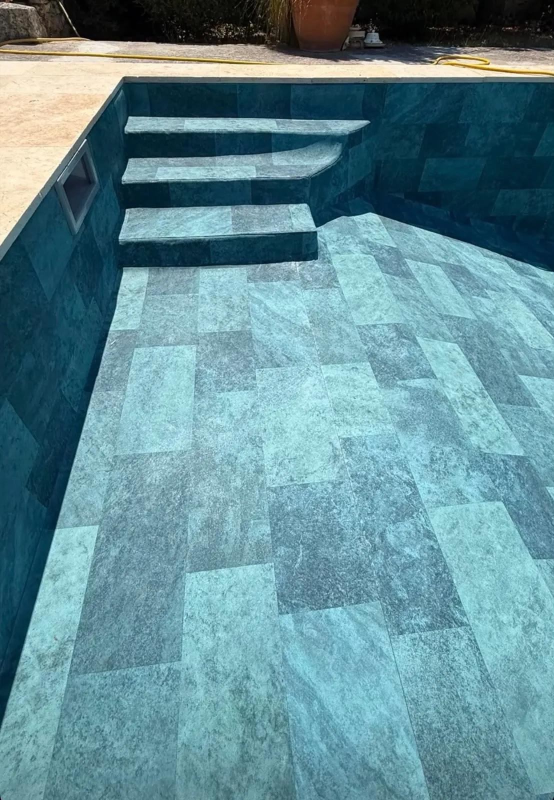 Bassin de piscine vide carrelé de grands carreaux vert-gris façon pierre, escalier d’angle carrelé, skimmer dans la paroi