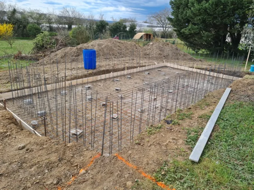 Fouille d’une piscine : ferraillage du fond posé sur cales, fers en attente pour les murs, planches de coffrage sur le pourtour
