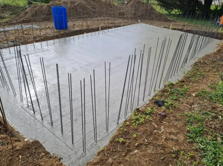 Fond de piscine en béton fraîchement coulé, fers à béton dressés en attente sur tout le pourtour