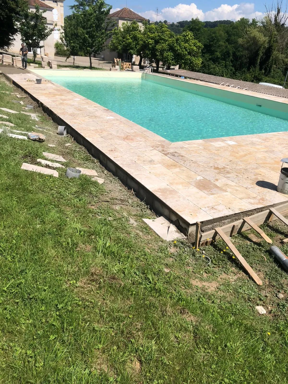 Piscine remplie bordée d’une plage en dalles de pierre, coffrage en bois encore en place au bord de la pelouse