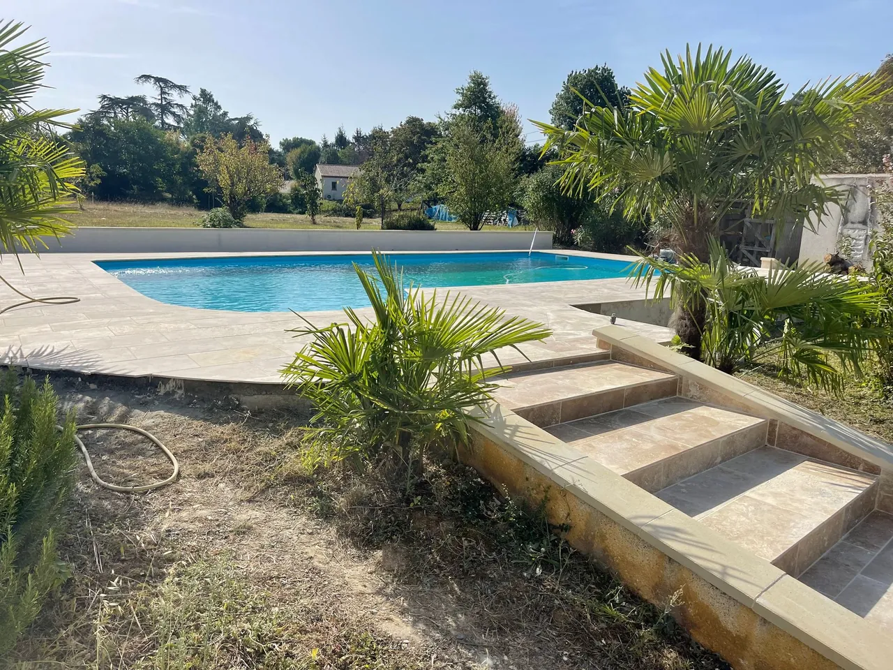 Piscine bordée d’une plage en dalles de pierre claire, escalier en dalles et palmiers