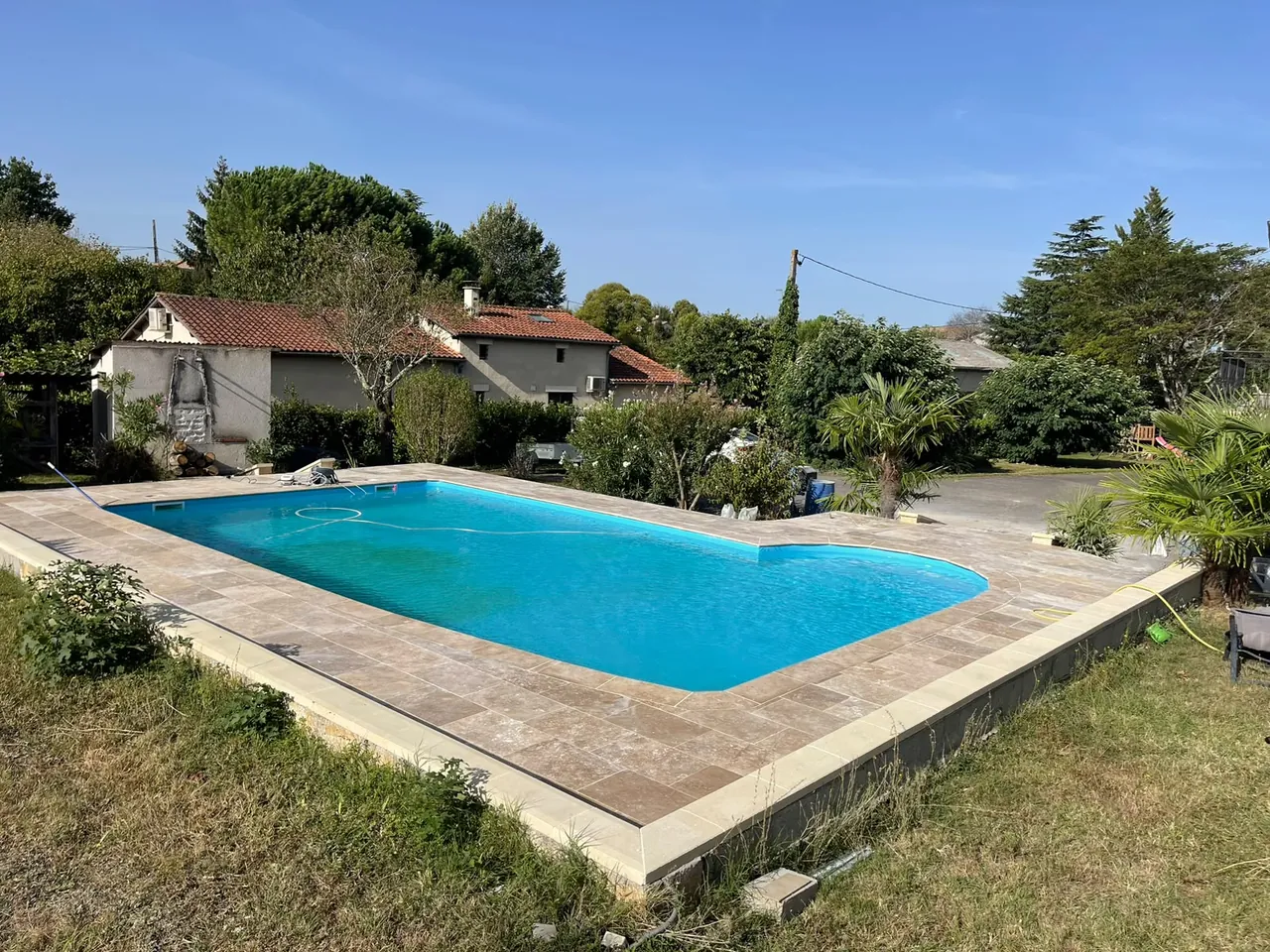 Piscine au liner bleu entourée d’une plage en dalles de pierre et d’une bordure coiffée, jardin et palmiers autour