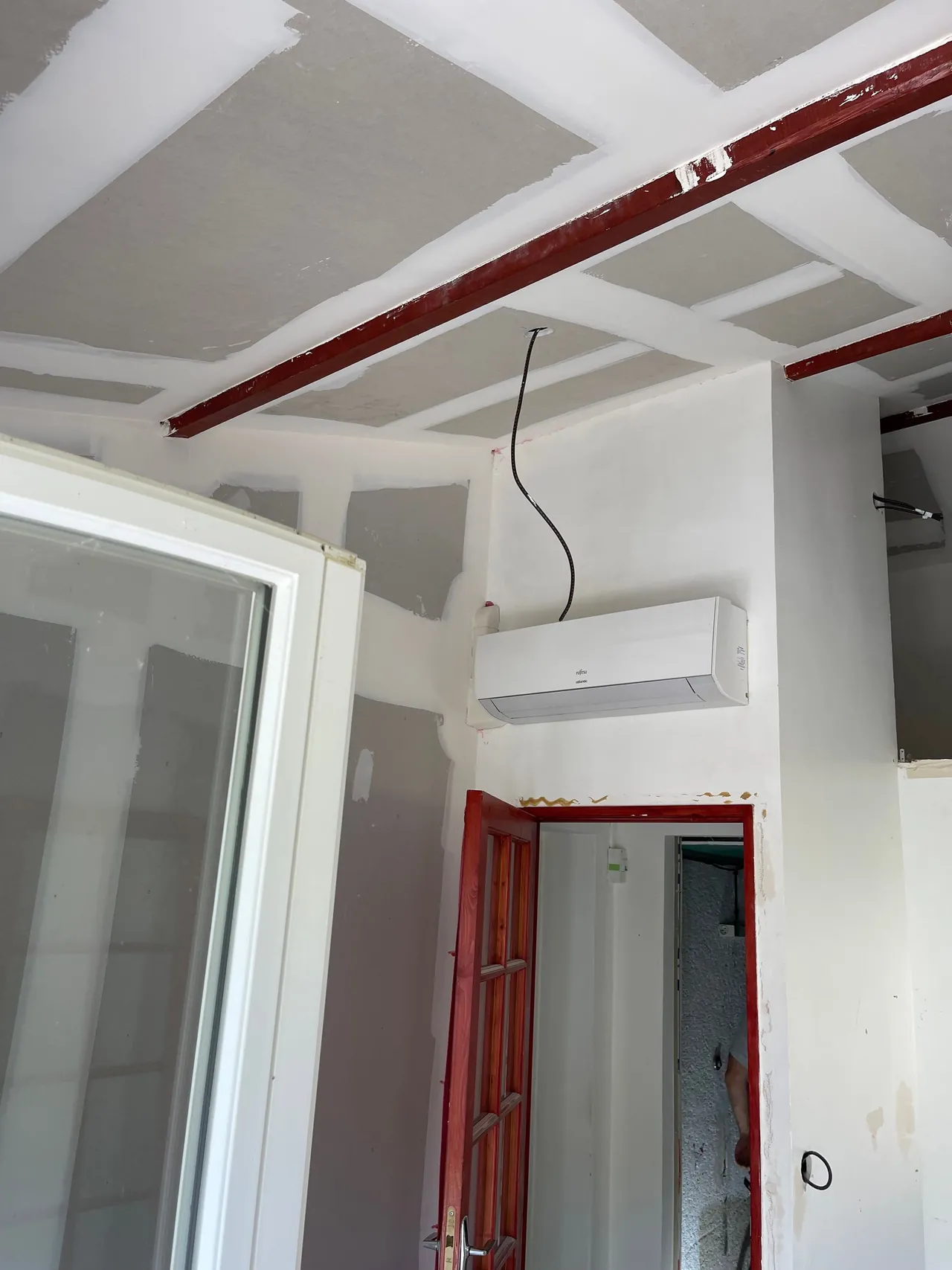 Plafond en plaques de plâtre jointées entre des poutres métalliques rouges apparentes, porte rouge au fond