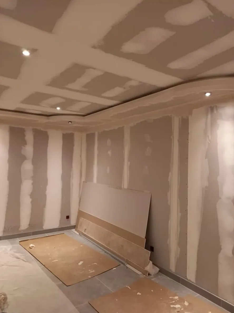 Pièce aux murs et au plafond en plaques de plâtre jointées, spots encastrés et faux plafond à décroché, plaques posées au sol