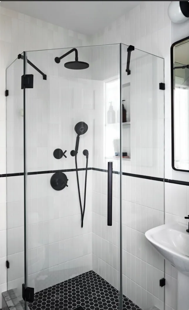 La même salle d’eau refaite : douche d’angle vitrée à profilés noirs, faïence blanche, sol en mosaïque noire