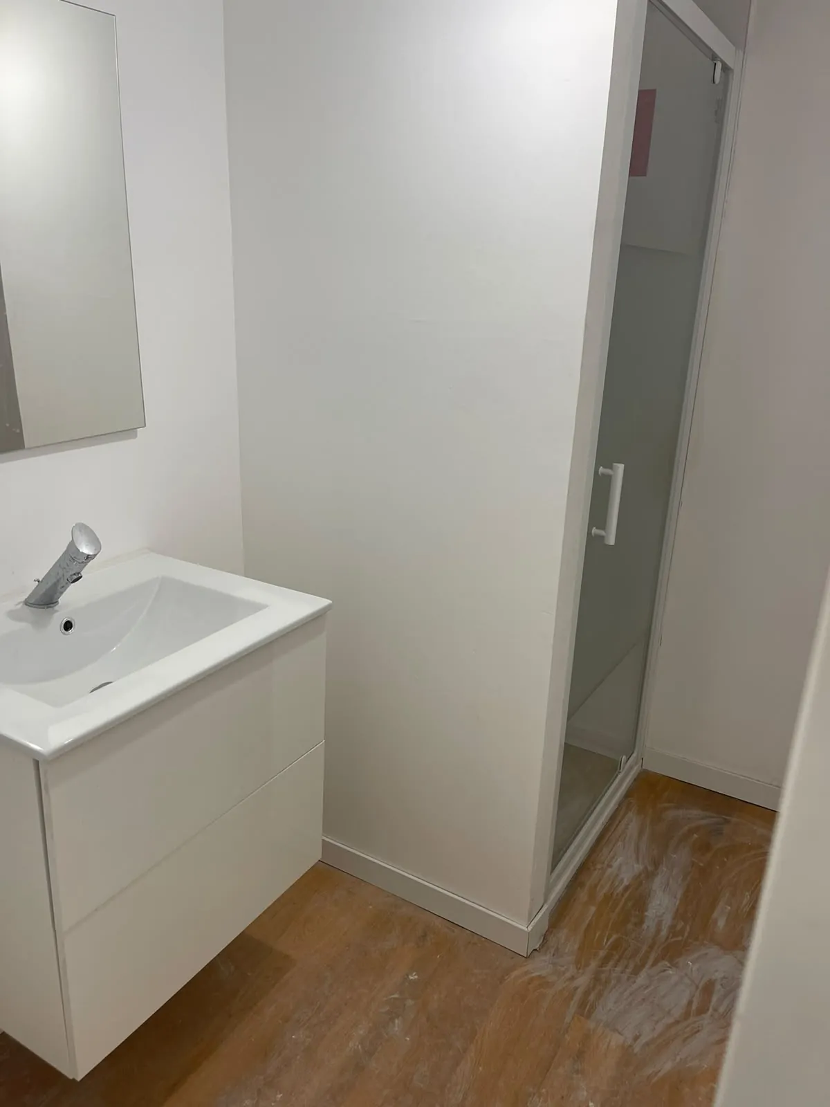 Salle d’eau en finition : meuble vasque blanc suspendu, porte de douche vitrée, sol encore poussiéreux