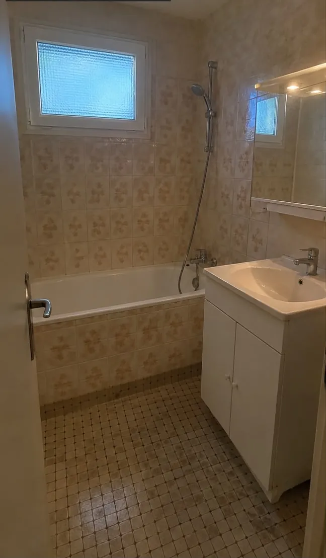 Salle de bains ancienne : faïence beige à motifs, baignoire, meuble vasque blanc, sol en petite mosaïque