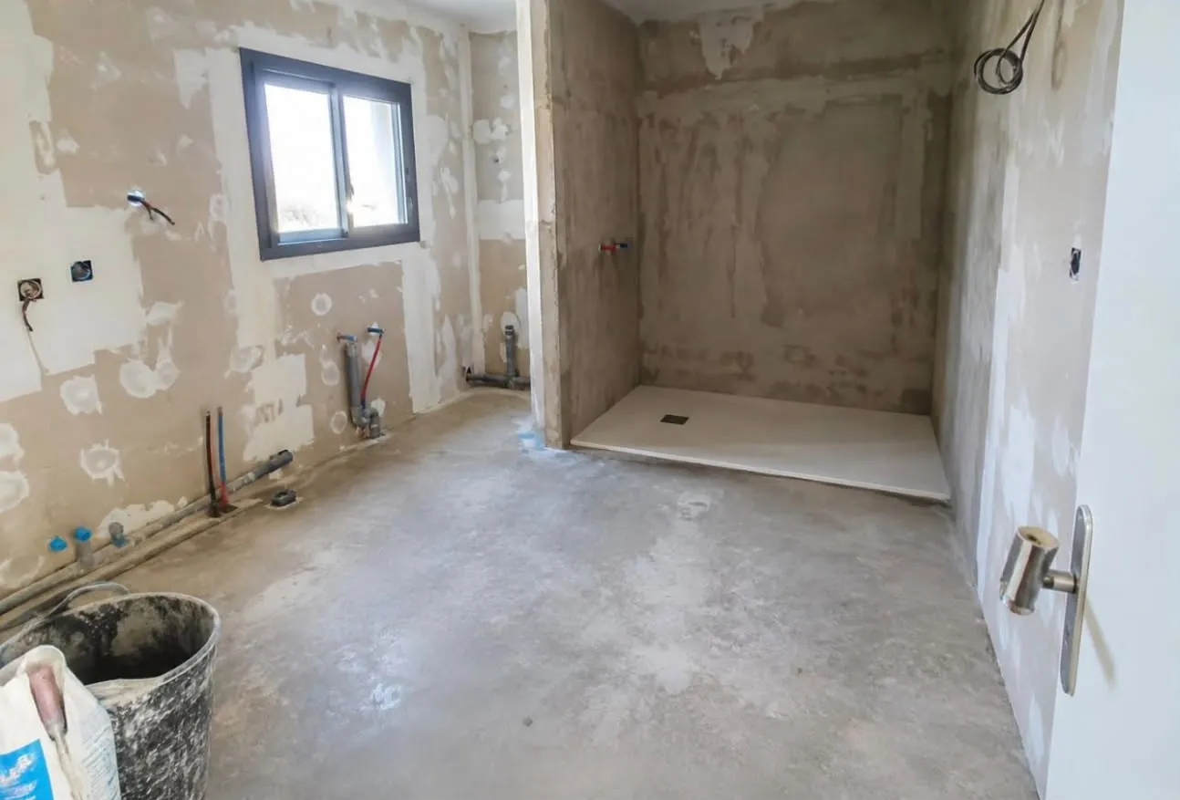 Salle de bains mise à nu : murs décapés, sol en chape, arrivées d’eau en attente, emplacement de la douche au fond