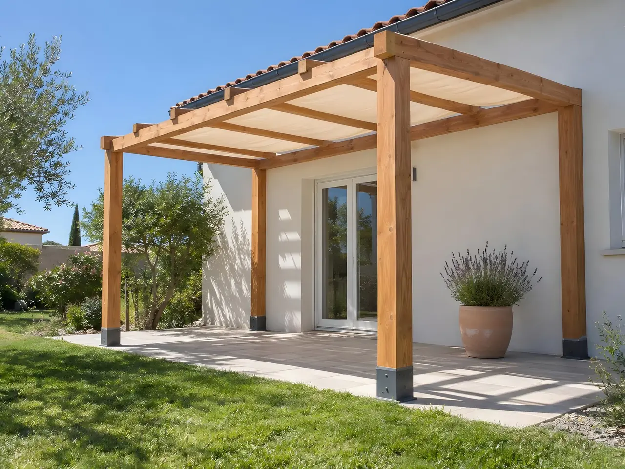 Pergola en douglas sur pieds métalliques adossée à une maison blanche, toile beige qui ombrage la terrasse dallée