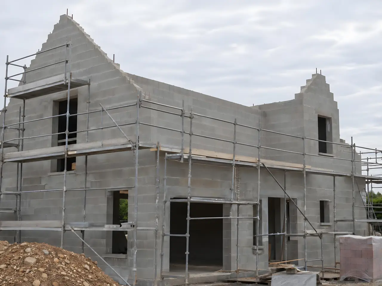 Maison neuve en parpaings sous échafaudage, pignons montés en pointe et toit encore ouvert sur le ciel