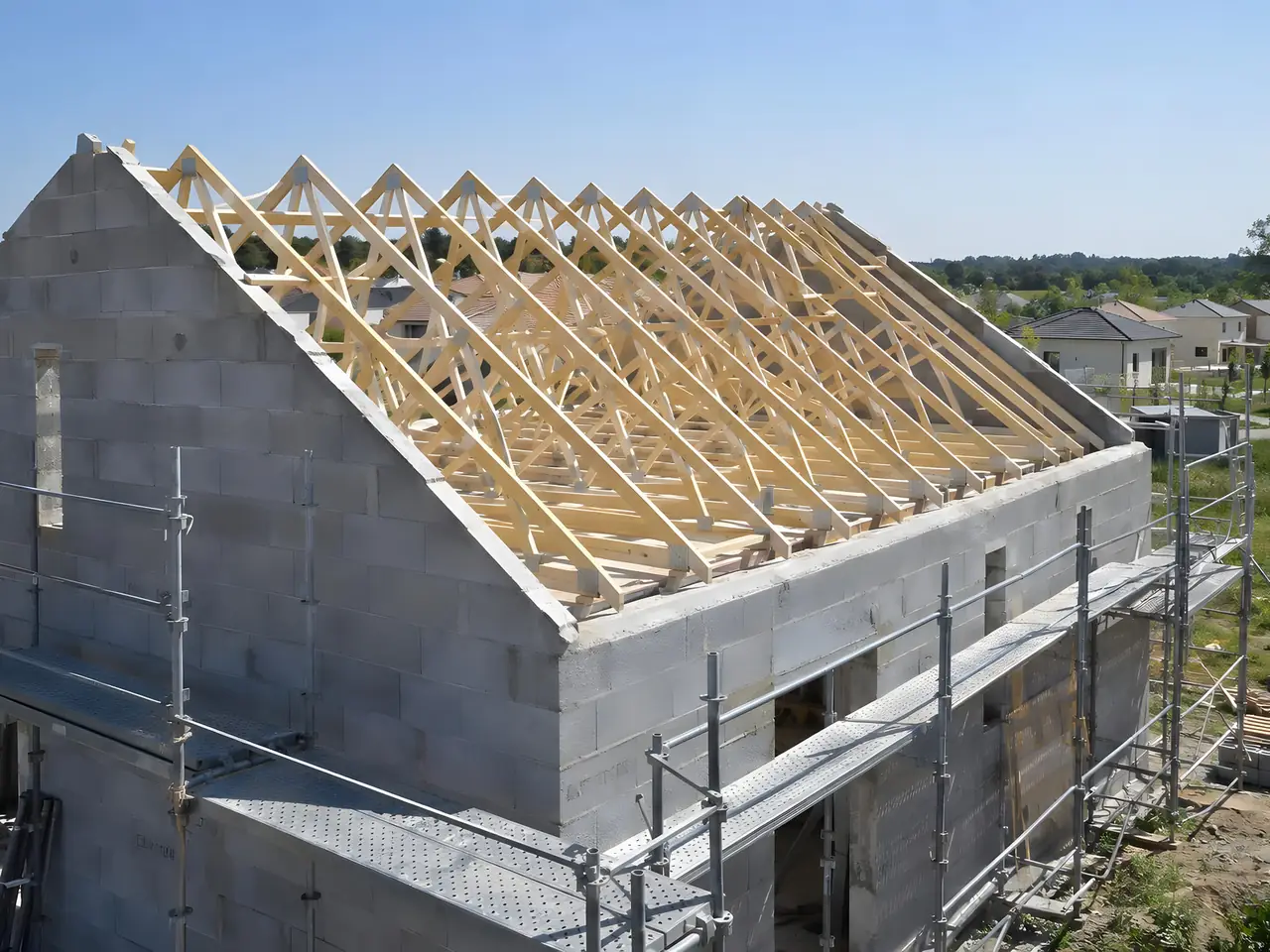 Pavillon neuf en parpaings sous échafaudage, avec sa rangée de fermettes en bois clair posées sur les murs
