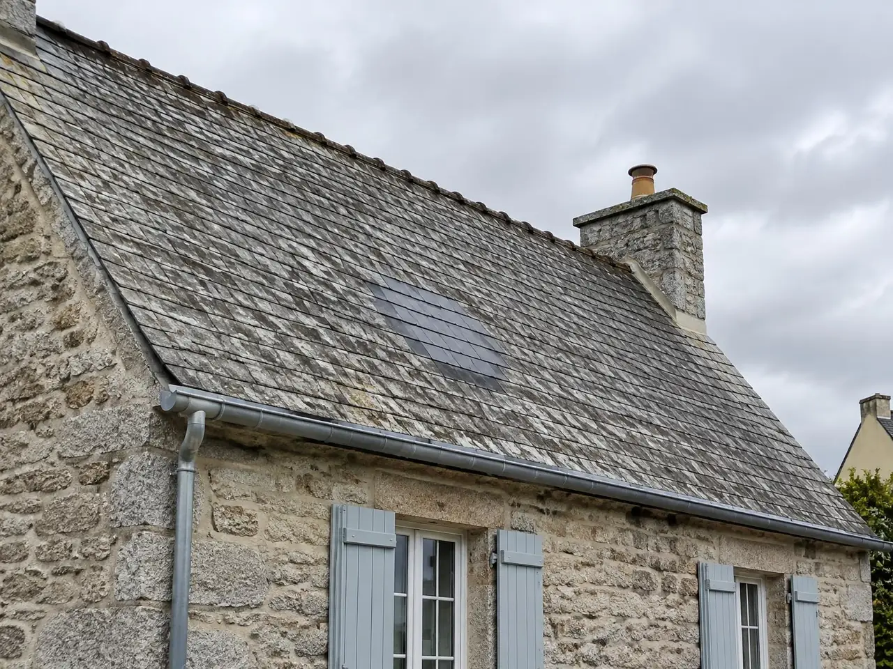 Toit d’ardoises anciennes d’une maison en pierre, avec une zone d’ardoises neuves plus sombres au milieu du pan