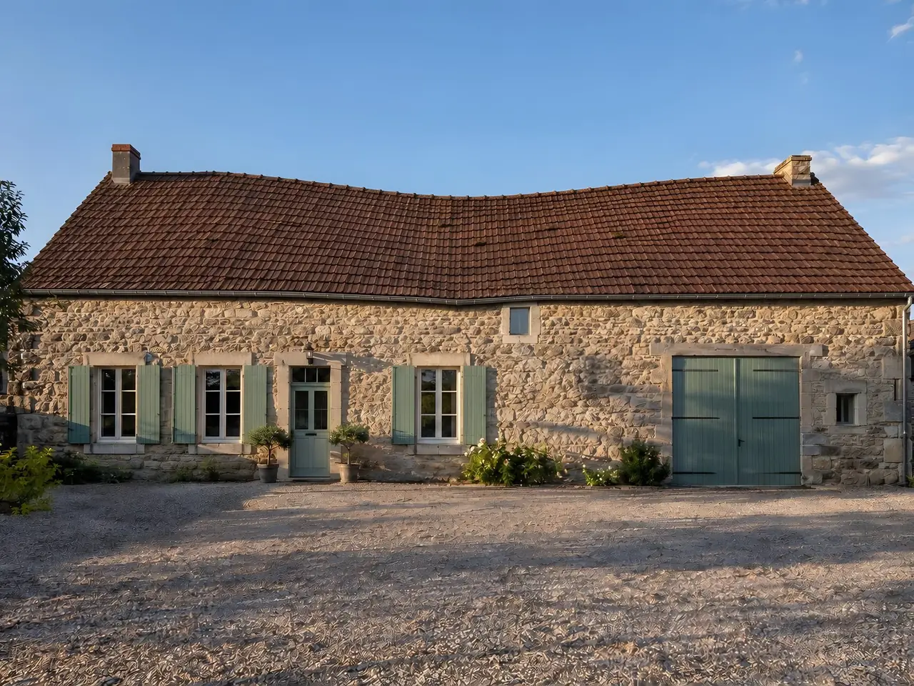 Longère en pierre aux volets vert pâle, long toit de tuiles brun-rouge creusé au milieu, faîtage affaissé en arc
