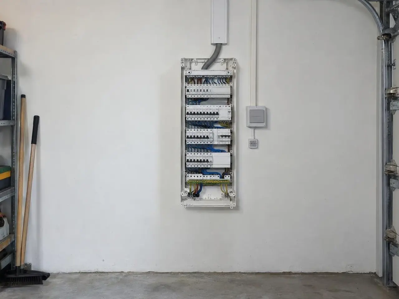 Tableau électrique neuf aux disjoncteurs alignés, câble qui remonte dans une goulotte blanche au mur du garage