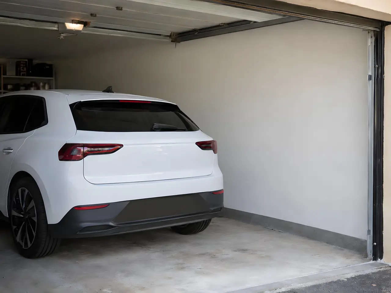 Garage ouvert : voiture électrique blanche garée devant un mur clair et nu, sans aucun point de recharge