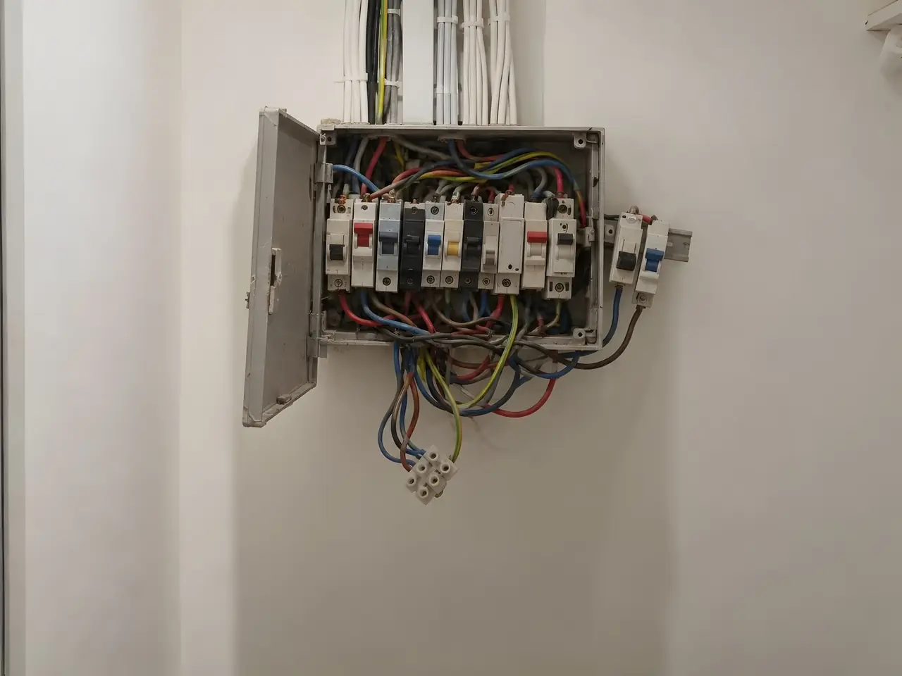 Vieux coffret électrique gris plein à craquer, porte pendante, fils de couleur en boucles, domino qui pend dessous