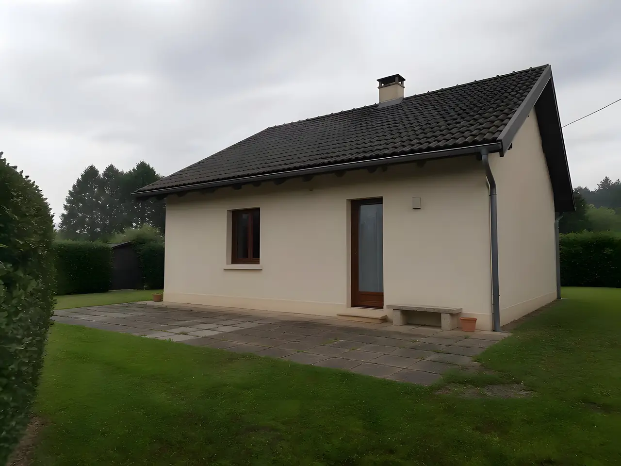 Maison de plain-pied à l’enduit crème vue du jardin, vieille terrasse en dalles, avant l’agrandissement