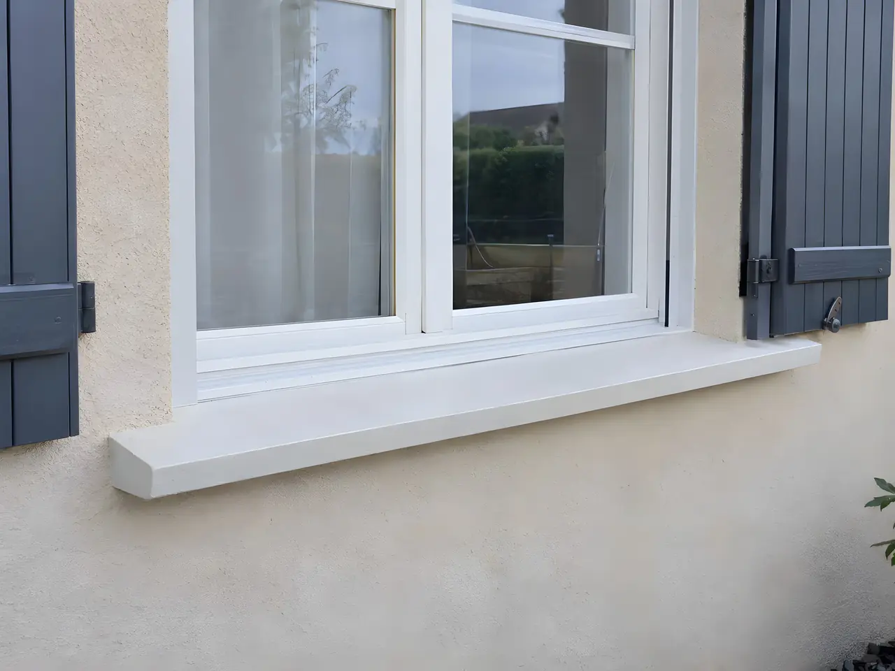 Appui de fenêtre neuf blanc et lisse sous une fenêtre à volets gris, enduit propre en dessous