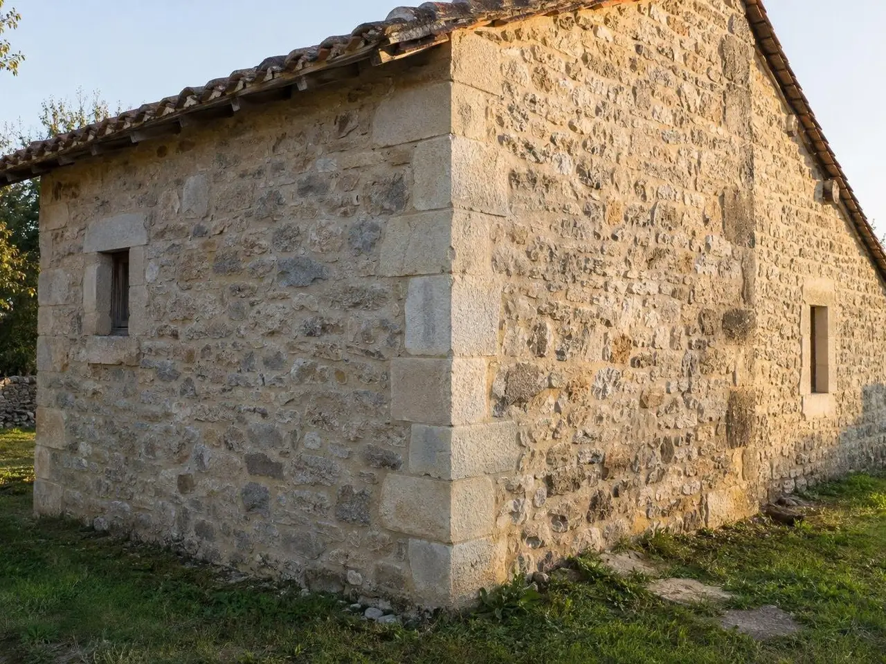 Angle d’une dépendance en pierre au toit de tuiles anciennes, pierres d’angle taillées alignées du sol au toit