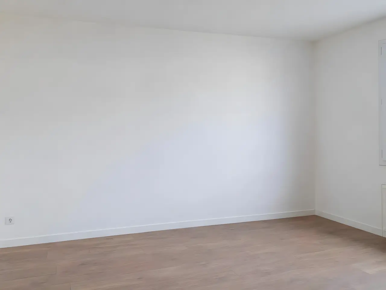 Mur de chambre lisse et blanc, d’un seul ton jusqu’à l’angle, au-dessus d’une plinthe blanche et d’un parquet