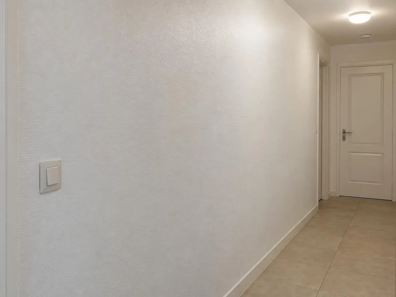 Mur de couloir couvert d’une toile de verre peinte en blanc satiné, trame fine et régulière, porte blanche au fond