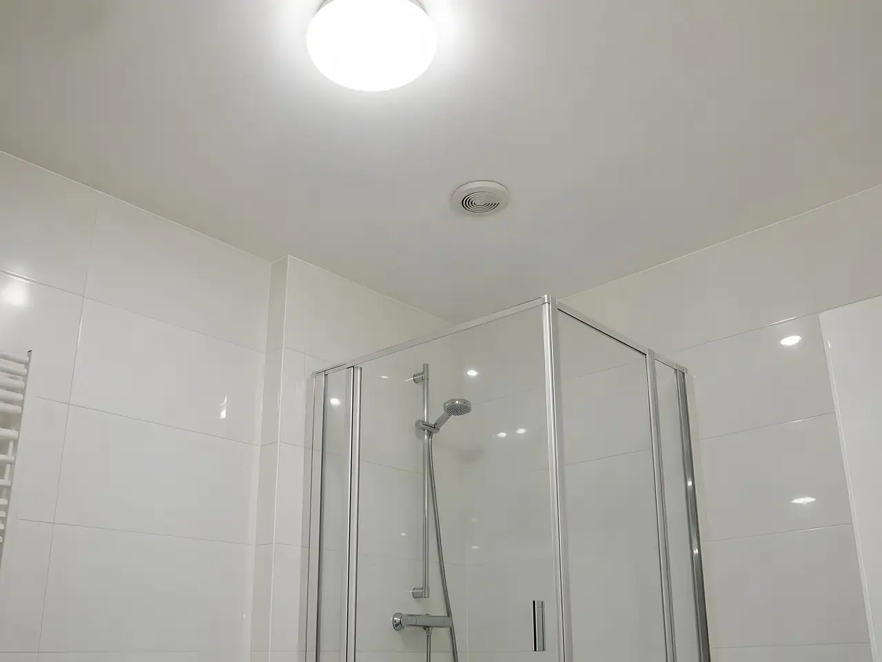 Plafond de salle de bains blanc net au-dessus d’une douche vitrée, bouche d’aération propre, faïence blanche