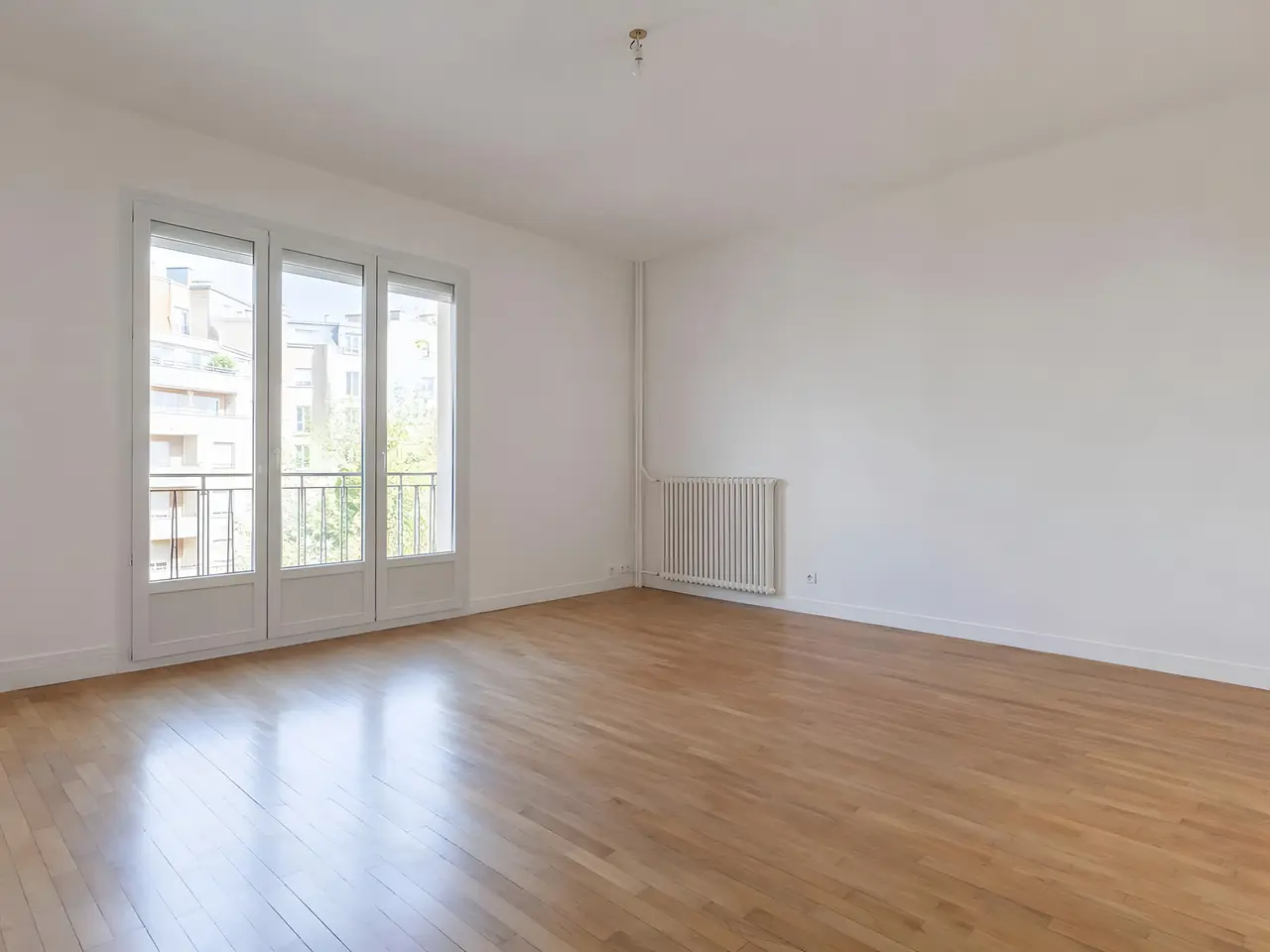 Séjour vide aux murs et au plafond d’un blanc net, grande porte-fenêtre lumineuse et parquet clair