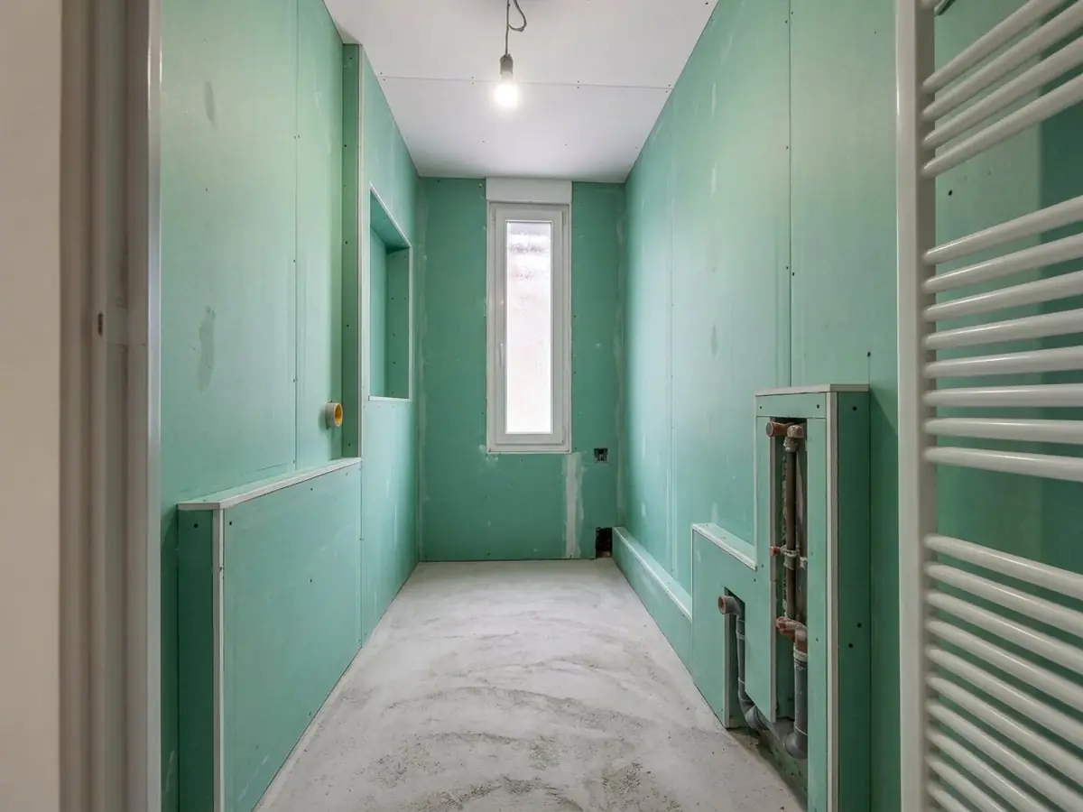 Salle de bains en plaques vertes avant le carrelage : niche, tuyaux en attente coffrés, petite fenêtre au fond