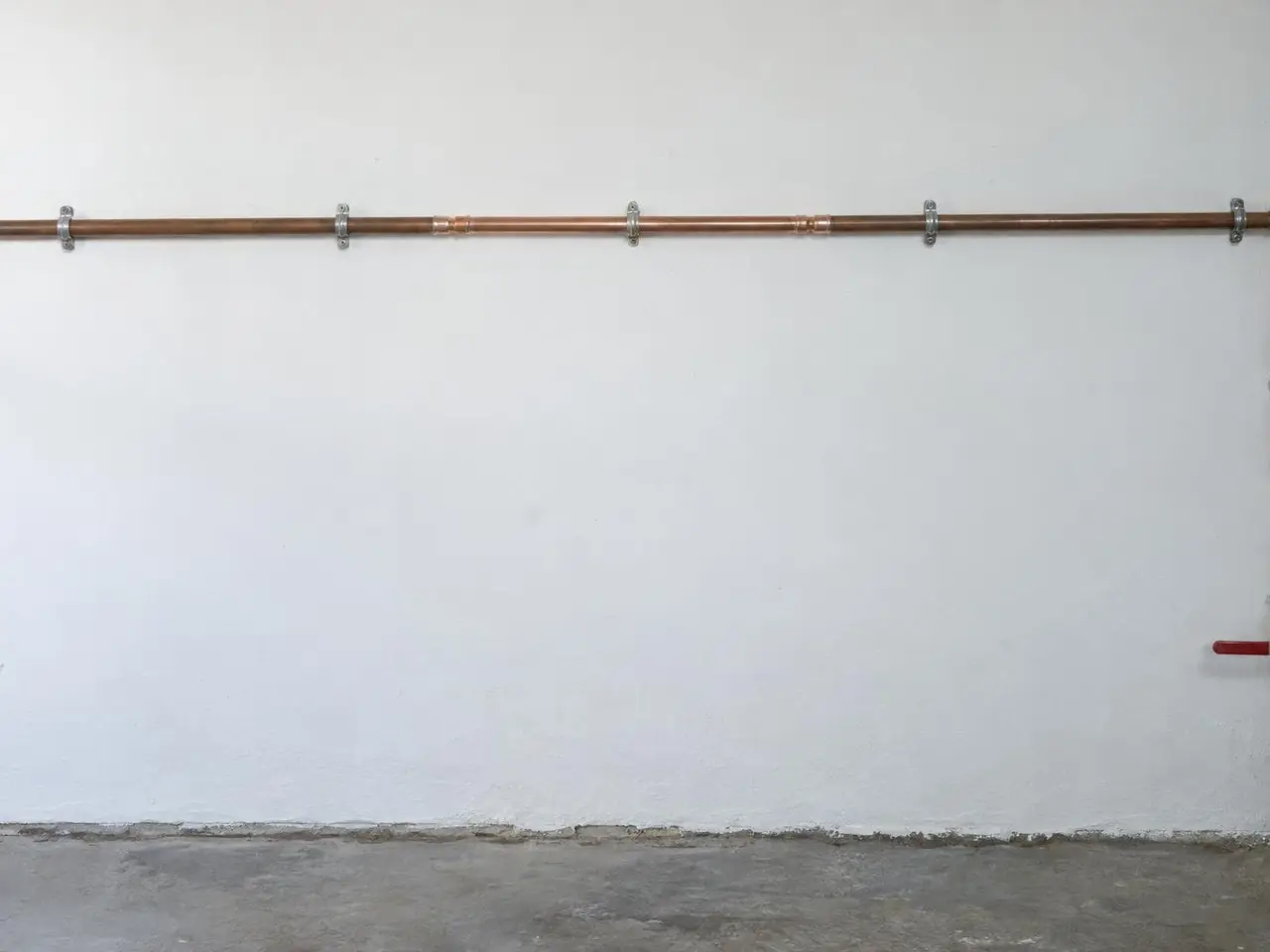 Tuyau de cuivre horizontal sur un mur blanc de garage, tronçon neuf raccordé par deux soudures, sol sec
