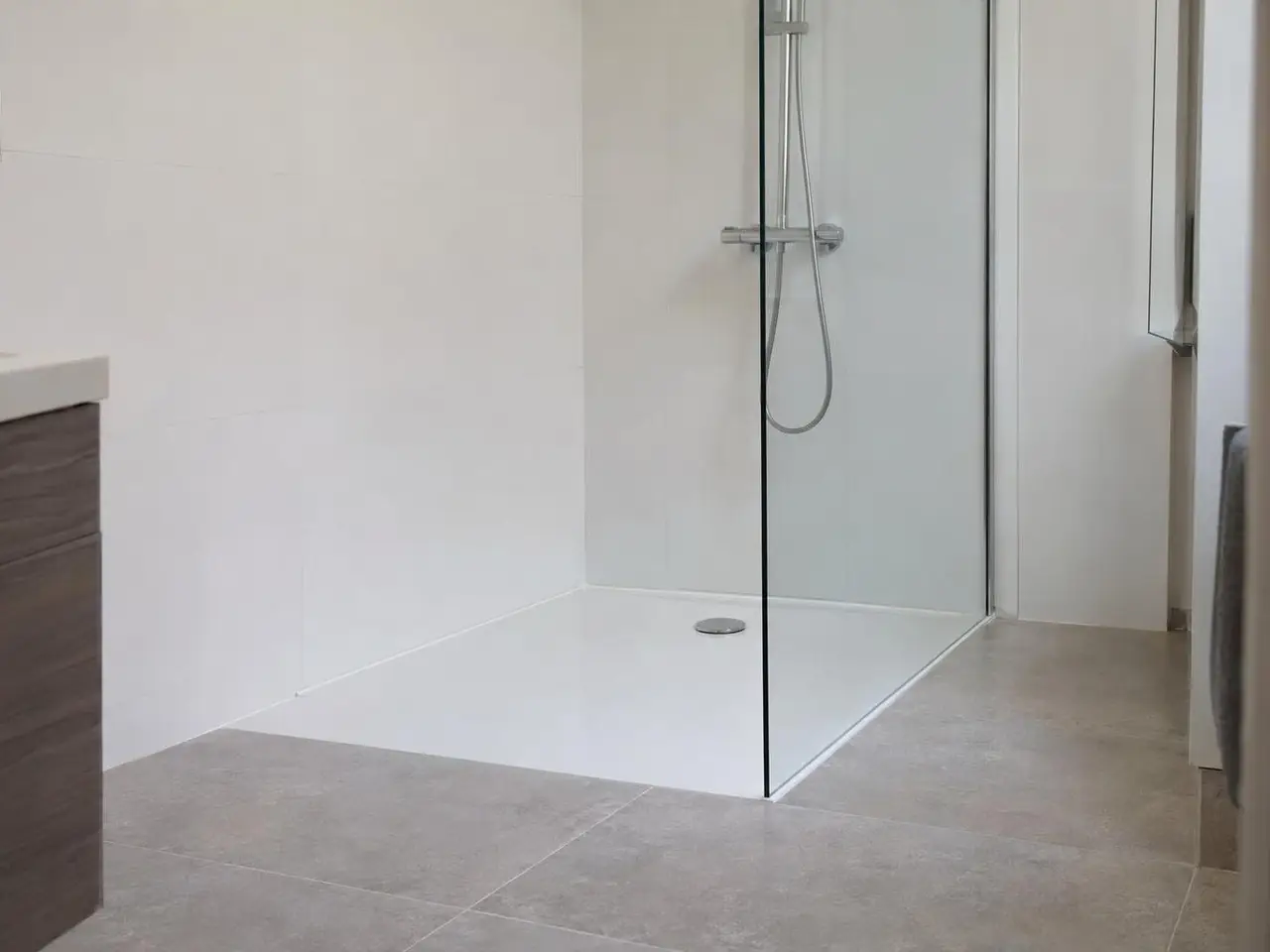 Salle de bains blanche, receveur de douche extra-plat au ras du sol gris, paroi vitrée fixe et mitigeur chromé