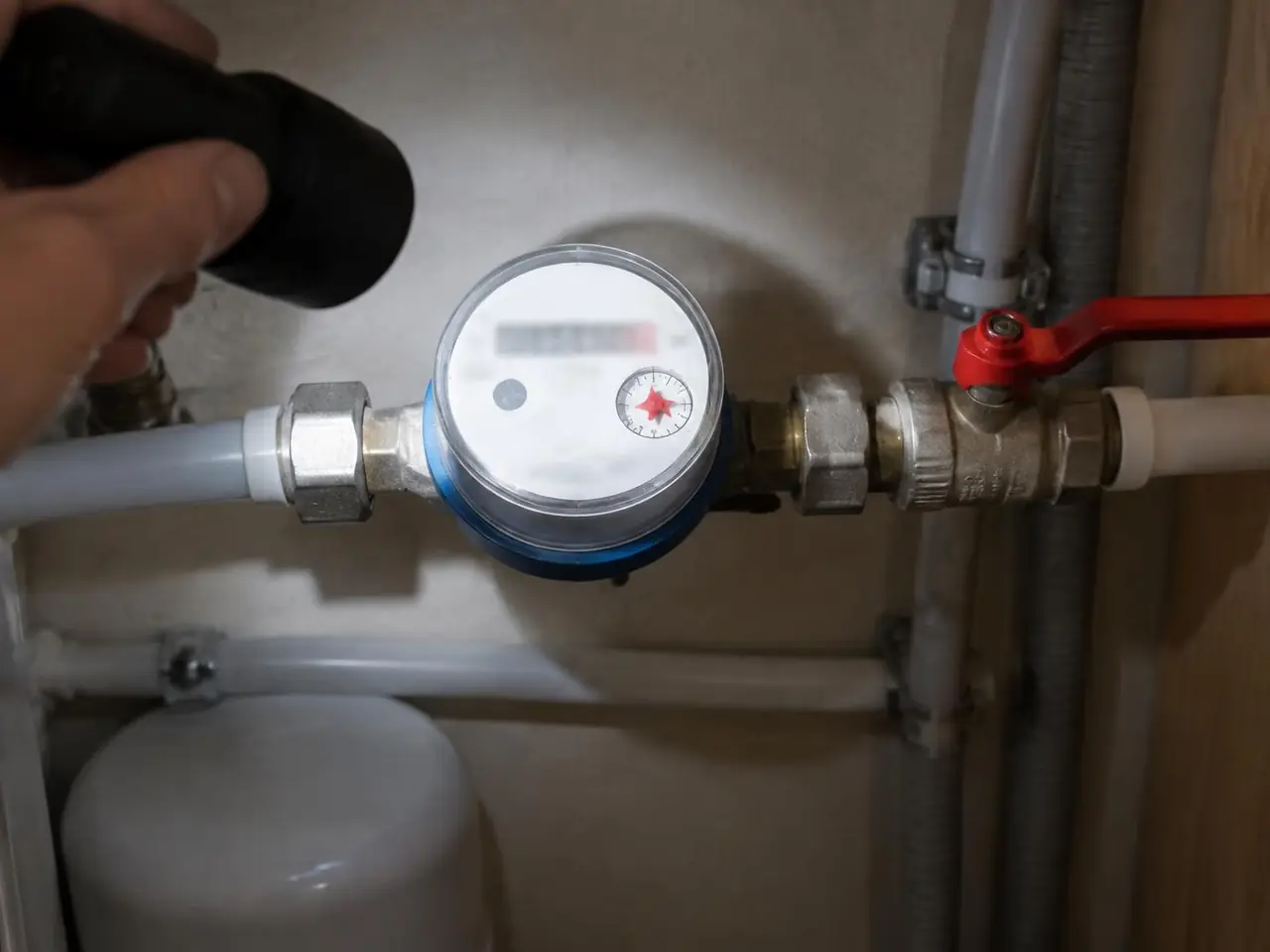 Lampe braquée sur un compteur d’eau, l’étoile rouge du cadran visible, robinet d’arrêt à manette rouge à côté