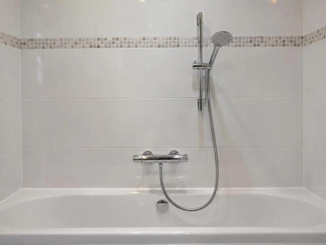 Mitigeur thermostatique chromé neuf au-dessus d’une baignoire blanche, flexible et douchette sur leur barre